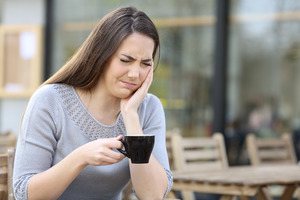 Woman holding coffee mug and rubbing jaw in discomfort